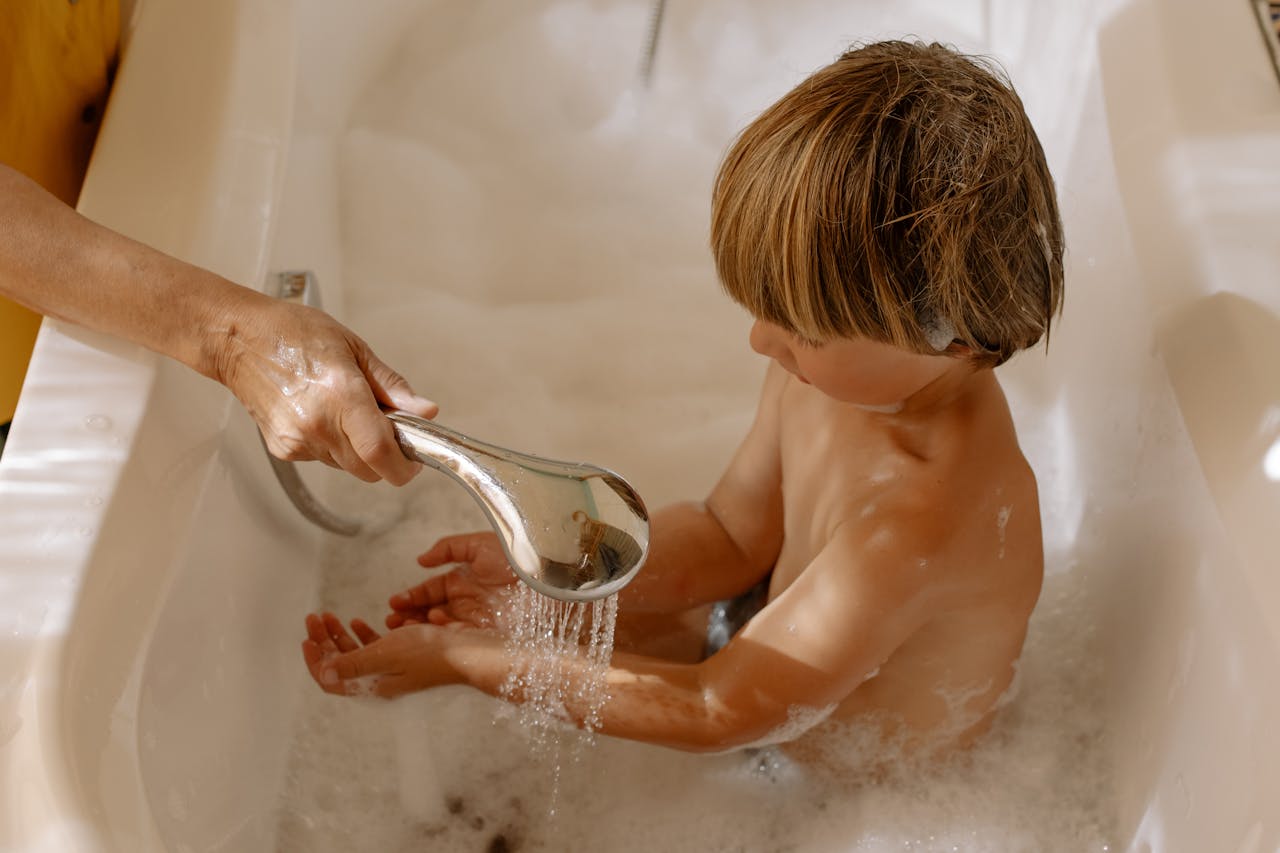 Young boy being washed by a parent in a bathtub, emphasizing hygiene and care.